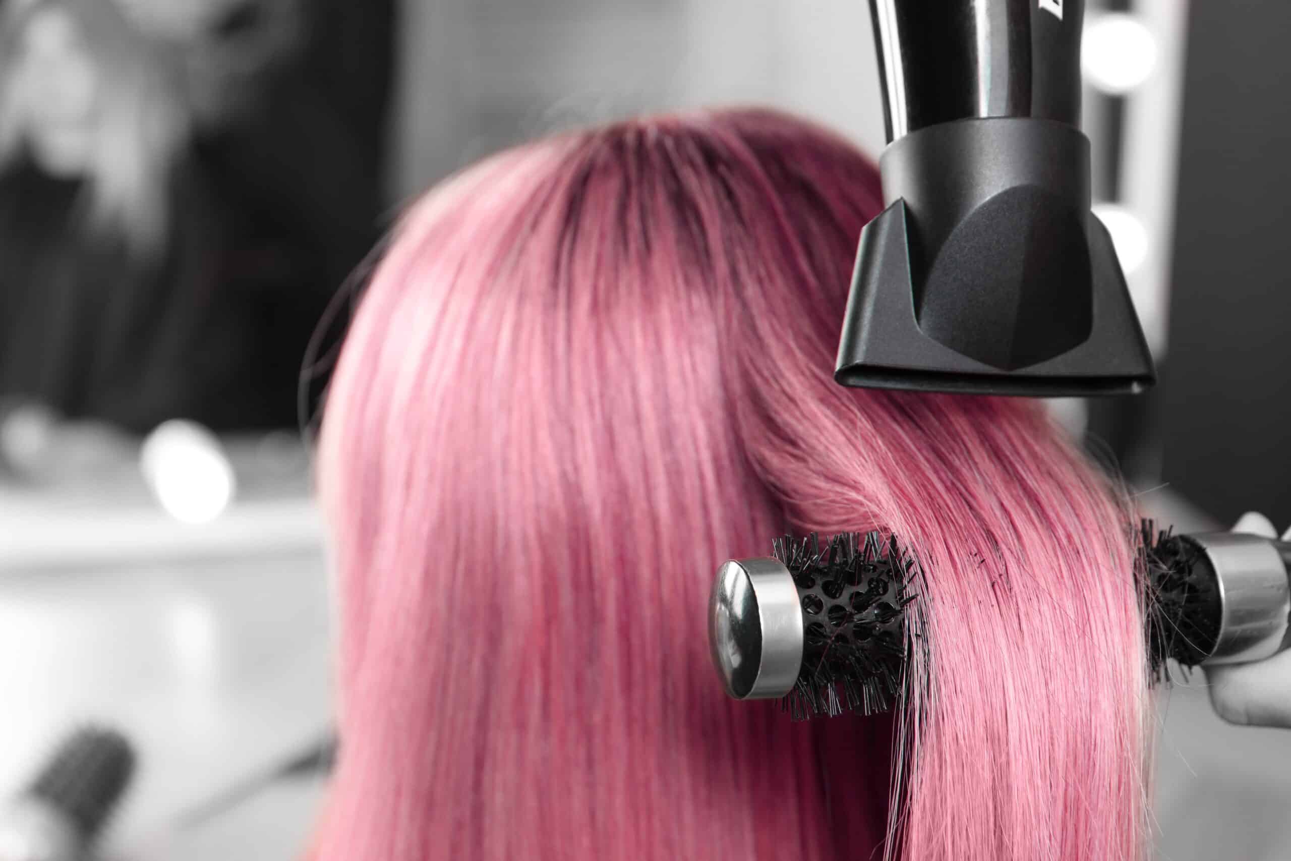 Brushing de cheveux roses avec un sèche-cheveux et une brosse ronde dans un salon de coiffure professionnel.