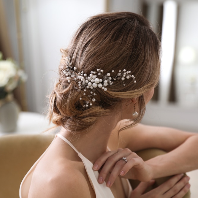 Coiffure de mariée avec un chignon bas élégant orné d'un peigne en perles et cristaux scintillants.